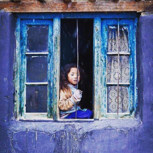 Girl sitting by the window in Kibber village, Spiti Valley, Himachal Pradesh