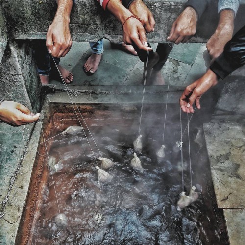 Devotees holding uncooked rice pouches in hot water spring for preparing rice in Manikaran. The temperature is high enough to boil rice, pulses, and vegetables. The naturally evolved spring has no minerals such as Iron or Sulphur in the water,